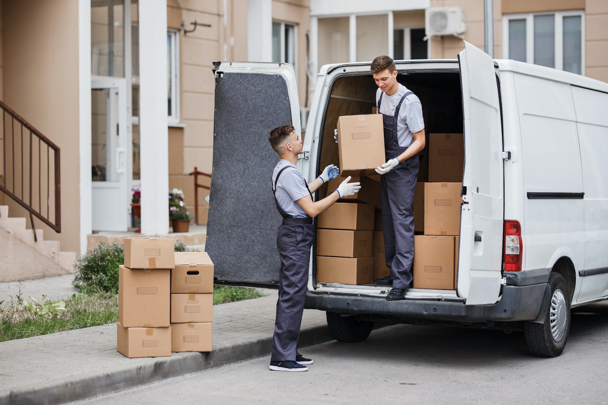 two young handsome movers wearing uniforms are unloading the van full of boxes house move mover 1 Tot Guardaet